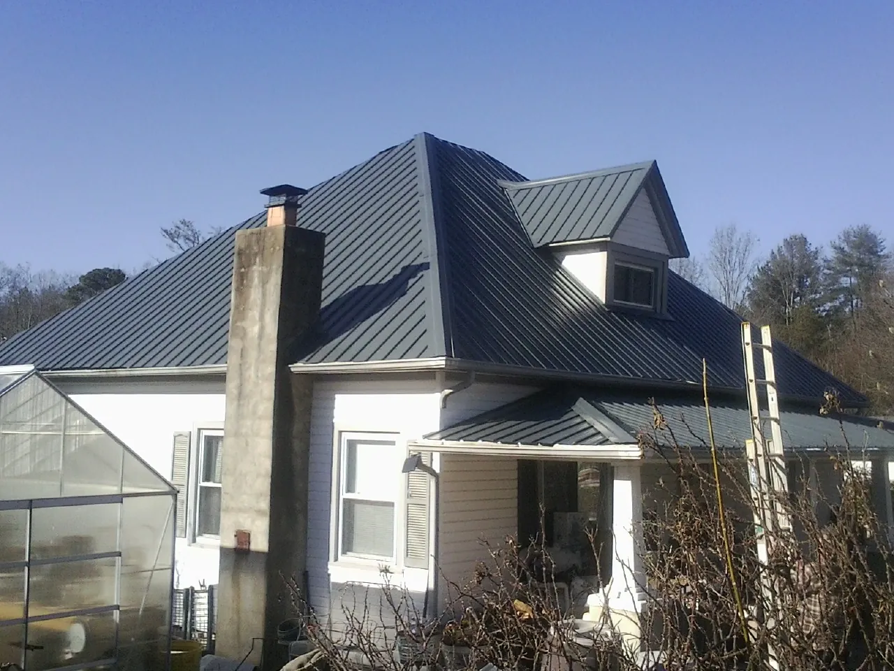 Dark blue standing seam metal roof on a white farmhouse with dormer — Slate & Tile Roof Repair by Roofing Brothers in Maxwell