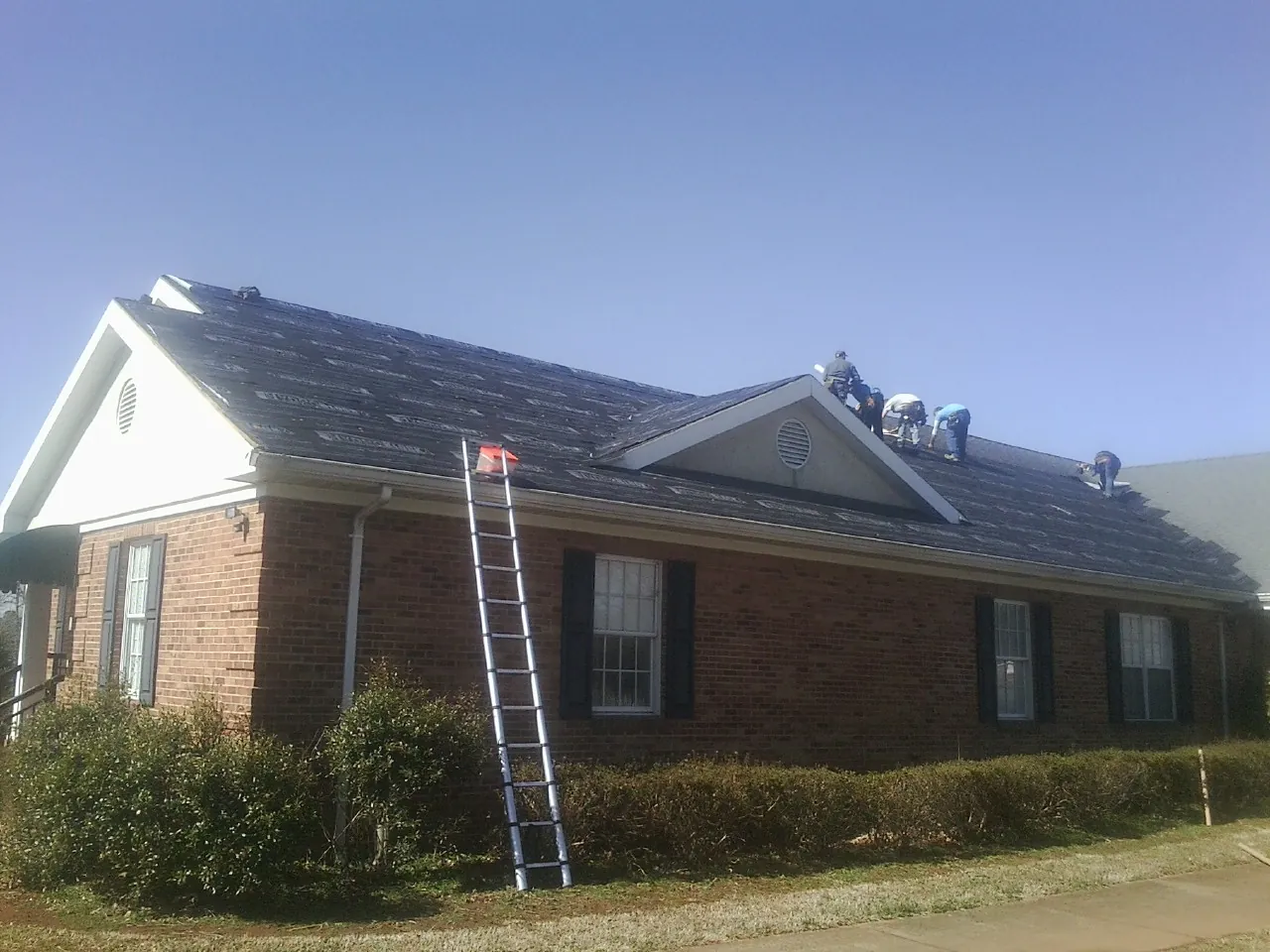 Crew tearing shingles off a brick ranch roof with a ladder set — Metal Roof Repair work by our crew in Maxwell