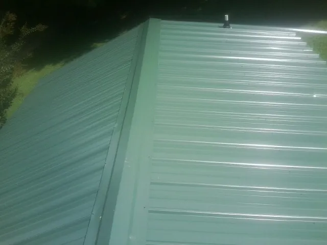 New green metal panels meeting at the ridge of a roof — Flat Roof Repair work by our crew in Maxwell